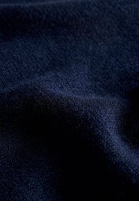 Tessuto blu navy con una superficie morbida e texture, caratterizzato da fibre fini e sottili variazioni di ombreggiatura, che indicano un materiale lavorato a maglia.