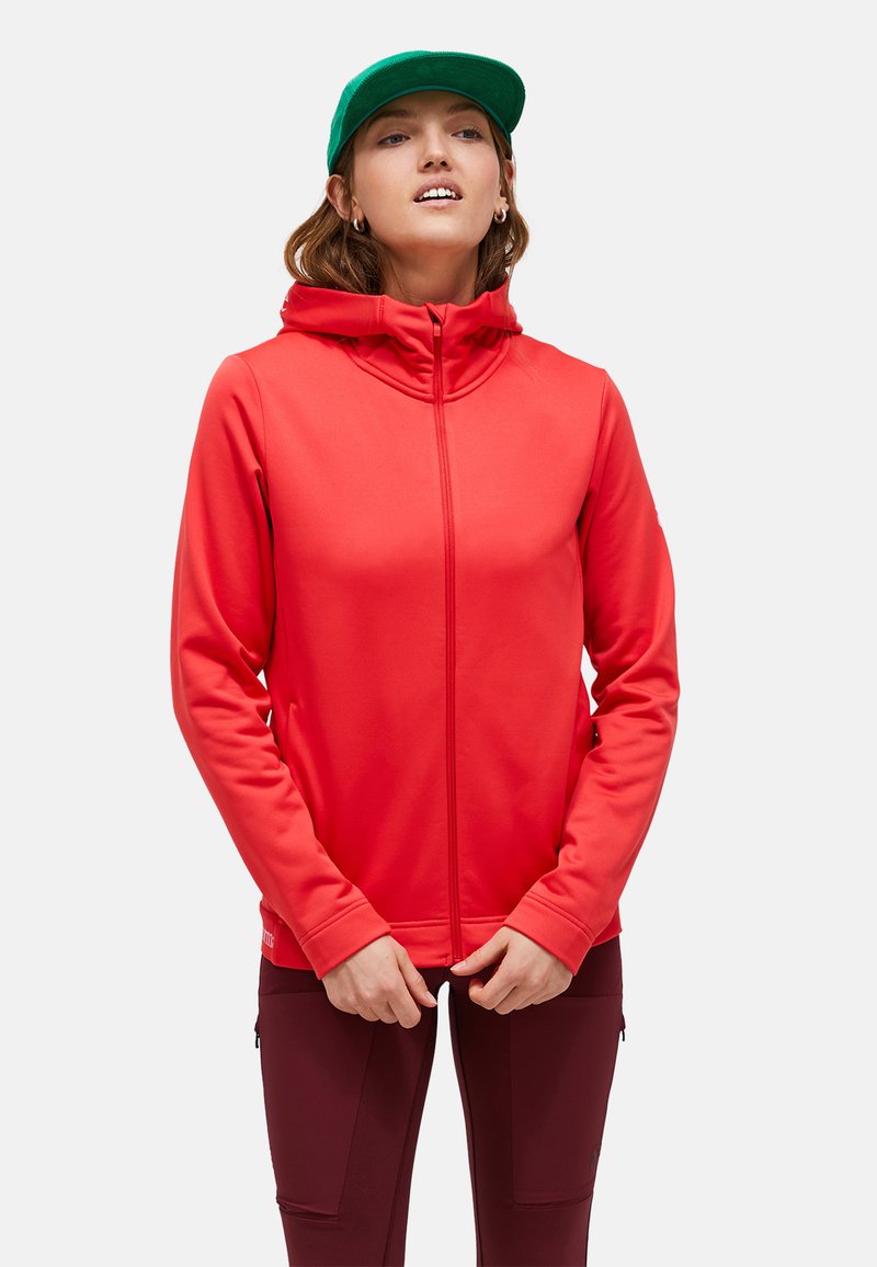 Rode zip-up hoodie met een hoge kraag, gemaakt van een gladde stof. Heeft een capuchon en lange mouwen. Draagt met bordeauxrode broeken en een groene pet.