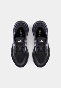 Chaussures de sport noires avec une tige en mesh agrémentée d'accents violets, un amorti léger et une semelle extérieure texturée pour une meilleure adhérence.