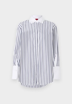 Camicia bianca con righe verticali blu navy, maniche lunghe con polsini bianchi, colletto classico e orlo curvo. Texture del tessuto liscia.