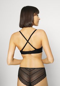 Black bralette with adjustable crossed straps and a hook closure. Paired with black lace hipster shorts featuring a chevron pattern.