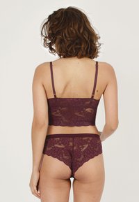 Kanten bralette en bijpassende slip set in diep bordeauxrood. Bevat bloemmotieven, verstelbare bandjes en golvende randen voor extra comfort.