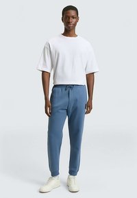 Niebieskie spodnie dresowe z elastycznym pasem i bocznymi kieszeniami, zestawione z białym t-shirtem. Spodnie mają naszywkę z logo na nogawce.