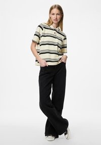 Korte mouw polo in lichtgeel met zwarte horizontale strepen, met een knoopsluiting bij de kraag. Gecombineerd met losse zwarte broek.