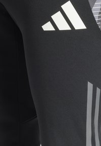 Zwarte sportleggings met witte en grijze adidas-logo's, een gladde textuur, een aansluitende pasvorm en een grafisch patroon aan de zijkant.