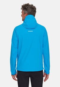 Blaue Softshell-Jacke mit Kapuze, verfügt über eine glatte Textur, elastische Bündchen und ein Logo auf der Rückseite. Leichtes Design, geeignet für den Einsatz im Freien.