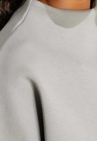 Felpa grigia chiaro realizzata in tessuto morbido e testurizzato, con collo alto e vestibilità comoda. I dettagli delle cuciture sono visibili lungo le spalle.