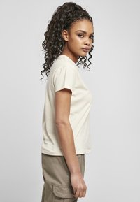 T-shirt in cotone beige chiaro con maniche corte, scollo rotondo e vestibilità rilassata, abbinato a pantaloni cargo verde oliva chiaro.
