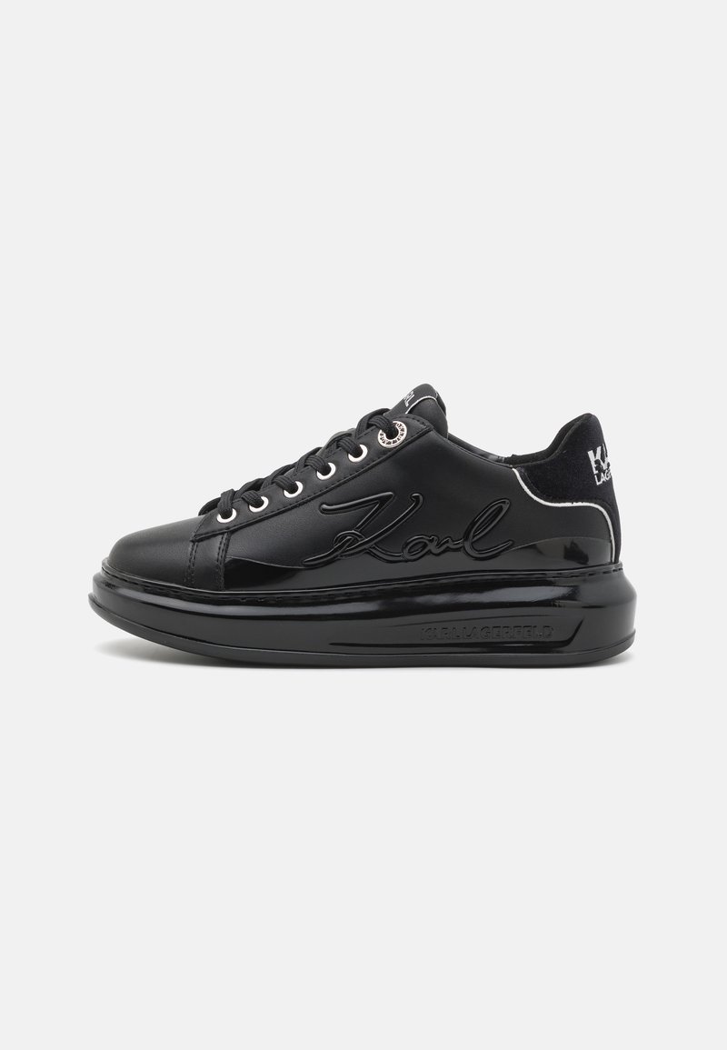 Black leather sneakers with a glossy finish, featuring a raised "Karl" logo, silver eyelets, and a textured heel accent. Flat sole design.