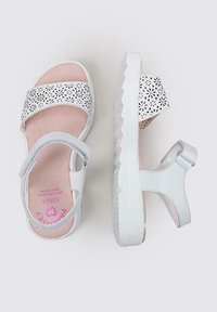 Sandalias blancas con un diseño floral perforado en las correas, plantillas acolchadas en color rosa y suela blanca texturizada con un patrón en zigzag.
