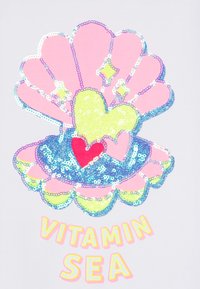 Sekojošs dizains ar sekvīnēm, kurā redzama rozā čaula ar zilām akcentām un dzeltena sirds, ko ieskauj teksts "VITAMIN SEA" spilgti dzeltenā krāsā.