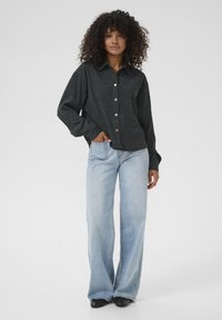 Schwarzes Hemd mit Knöpfen und Kragen, ausgestattet mit Metallknöpfen, kombiniert mit hellblauen, weit geschnittenen Jeans. Glatte Stoffoberfläche.