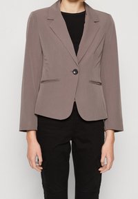 Grå blazer i lätt tyg, med en knappstängning, slagkrage och två framfickor. Modellen har matchat den med en svart topp.