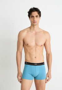 Boxers en coton bleu avec une ceinture noire portant le nom de la marque. Le design est ajusté, avec une texture lisse et sans motifs.