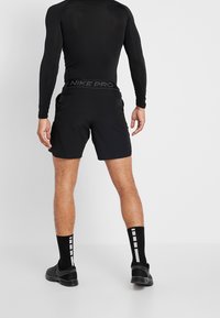 Svart träningsoutfit bestående av en långärmad topp och shorts, med en märkesinspirerad midja. Texturerad tyg och figurnära design. Svarta sportstrumpor.