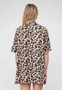 Vestito camicia con stampa leopardata e maniche corte; presenta una base beige chiaro, macchie marrone scuro e nere, e un taglio rilassato.