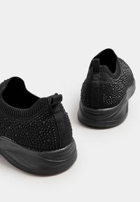 Baskets noires avec une tige texturée ornée de strass noirs décoratifs, ouvertures élastiques et une semelle en caoutchouc pour le soutien.