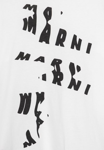 Camiseta blanca con letras abstractas en negro que presentan formas irregulares, creando una apariencia estratificada y texturizada en la tela.