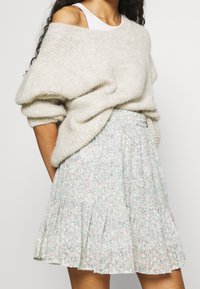 Maglione grigio chiaro oversize in maglia con maniche voluminose abbinato a una gonna lunga a fiori pastello con volant e una vita elasticizzata.