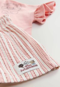 Tissu rayé rose et blanc avec patch brodé montrant trois visages de chats et texte "The Aristocats" sur un vêtement plié.