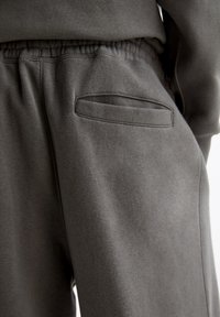 Grijze sweatpants van een zachte stof met een elastische tailleband en een subtiele schuine pocket. De stof heeft een gladde textuur en minimale naden.