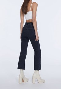 Mörk denim jeans med hög midja, croppad rak ben och fransad fåll; parat med vita plattform ankelstövlar och en åtsittande vit topp.