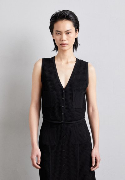 Vestido negro de punto sin mangas con escote en V, caracterizado por botones frontales y dos bolsillos de parche. Tejido texturizado con una silueta ajustada.