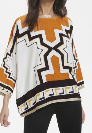 Top oversize con motivo geometrico in arancione, bianco e nero, con una bordatura dorata attorno al collo e all'orlo.