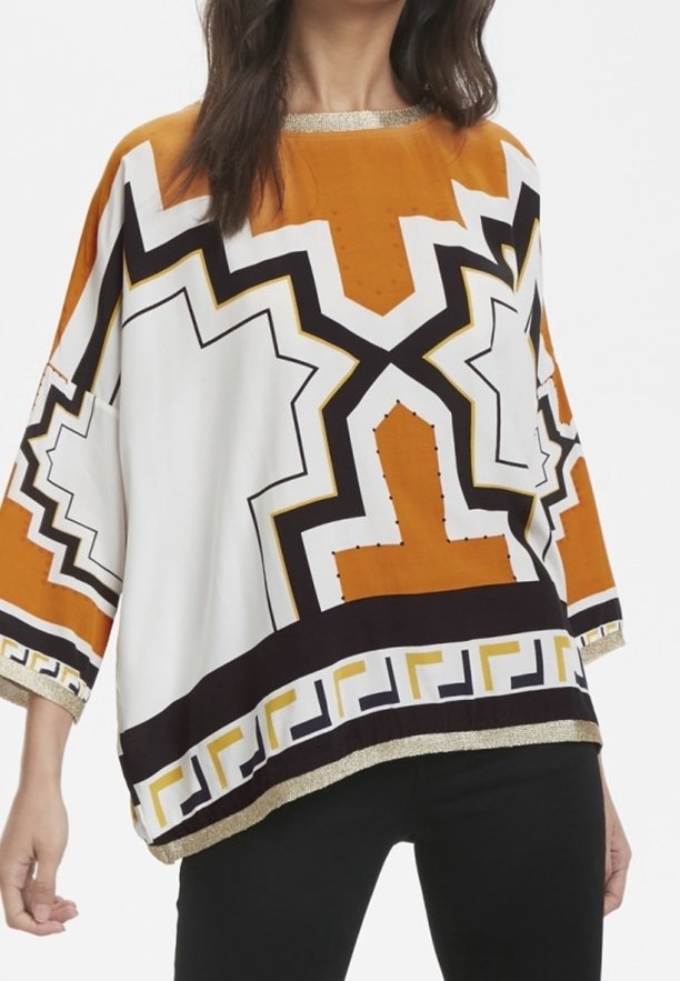 Top oversize con motivo geometrico in arancione, bianco e nero, con una bordatura dorata attorno al collo e all'orlo.