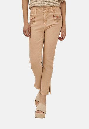 Jeans de mezclilla ligeros color durazno con bordado floral decorativo en los bolsillos, corte ajustado y dobladillos con abertura. Combinados con sandalias de plataforma beige.