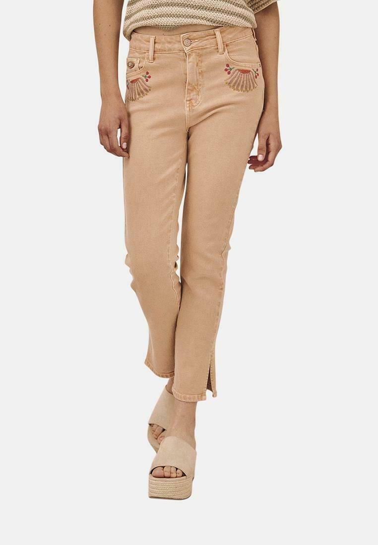 Jeans de mezclilla ligeros color durazno con bordado floral decorativo en los bolsillos, corte ajustado y dobladillos con abertura. Combinados con sandalias de plataforma beige.