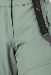 Grønne sports shorts lavet af et glat, let materiale. Funktioner inkluderer en sidelomme med lynlås og justerbare stropper med branding.