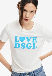 T-shirt bianco in cotone con lettere blu in grassetto "LOVE DSGL" accompagnate da un simbolo a forma di cuore, con scollo rotondo e maniche corte, realizzato in una vestibilità rilassata.