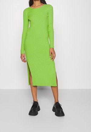 Robe à manches longues en côtes de couleur vert vif, avec des fentes sur les côtés pour un style supplémentaire. Assortie à des chaussures noires chunky.