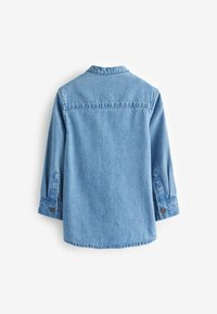 Camisa de mezclilla azul con cuello, mangas largas y puños de botón. Textura suave con un acabado ligeramente descolorido y dobladillo curvado en la parte inferior.