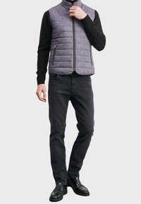 Padded vest w fioletowej, teksturowanej tkaninie, z wysokim kołnierzem, zamkiem błyskawicznym z przodu oraz dwiema bocznymi kieszeniami, w komplecie z czarnymi spodniami i butami.