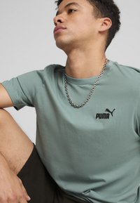 Světle zelené tričko s kulatým výstřihem vyrobené z měkkého materiálu, s malým černým logem Puma na hrudi a krátkými rukávy.