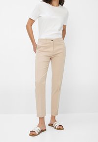 Chino beiges avec une coupe slim et une texture lisse, dotés d'une taille standard et d'une fermeture à un bouton. Associés à un T-shirt blanc et des sandales légères.