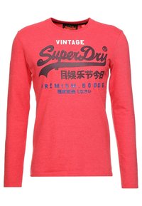 Czerwona koszulka z długim rękawem i okrągłym dekoltem z nadrukiem "Vintage SuperDry Premium Goods" oraz japońskimi znakami z przodu.