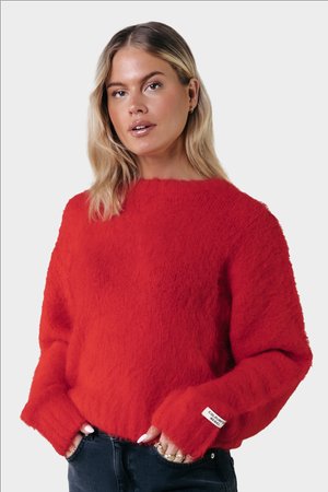 Red knitted sweater with a fluffy texture, wide neckline, and long sleeves. Features a tag on the cuff with brand name.