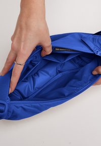Borsa in nylon blu con chiusura a zip. L'interno presenta scomparti imbottiti e una texture liscia. Una mano la tiene aperta per mostrarne il contenuto.