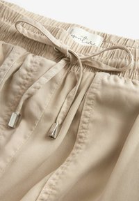 Beige lette shorts med elastisk livvidde, justerbar snor og metalspidser. Teksturert stof med lodrette striber.