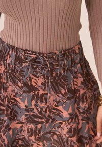 Top marrón de canalé combinado con una falda fluida de estampado floral en tonos burdeos, gris y óxido, con detalle de cintura ajustable.