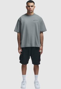 Grå oversized T-skjorte med rund hals og kort ermer, sammen med svarte cargo-shorts med sidelommer, og hvite sneakers.