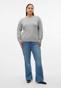 Un pull en maille gris à col rond associé à un jean flare bleu clair avec des fentes sur le bas, porté avec des chaussures noires à bout pointu.