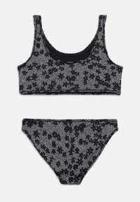 Μαύρο σετ μπικίνι με λευκό πουά λουλουδάτο μοτίβο, που περιλαμβάνει τοπ με στρογγυλή λαιμόκοψη και αντίστοιχο κάτω μέρος με ψηλό κόψιμο, τοποθετημένα επίπεδα πάνω σε λευκό φόντο.