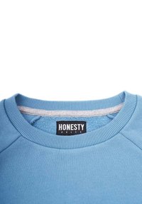 Sininen collegepaita, jossa on pyöreä kaula-aukko, resorit hihansuissa ja helmassa. Sisäkauluksessa on harmaata kangasta. Lappu lukee "HONESTY RULES" mustalla.