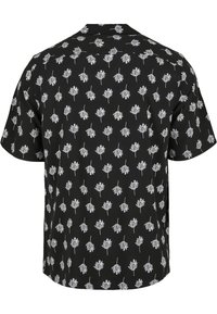 Chemise noire à manches courtes avec un motif répétitif de feuilles blanches. Fabriquée en tissu léger, avec une coupe décontractée et un col ouvert.