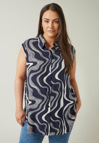 Marinblå ärmlös skjorta med ett vitt vågmönster, knäppning fram och en avslappnad passform med rundad nederkant. Mjuk tygstruktur.