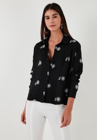 Black shirt with white floral print, button closure, and a relaxed fit. Features long sleeves and a collar. Smooth fabric texture.